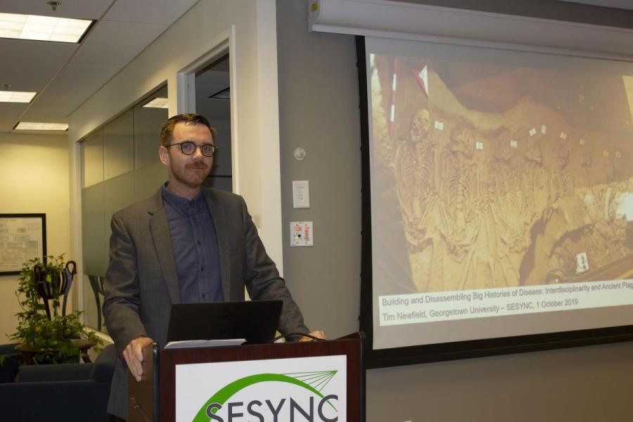 Tim Newfield stands behind a podium while giving a presentation